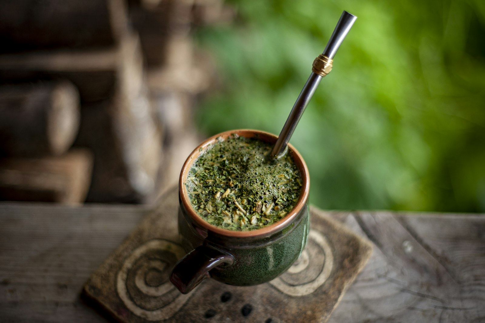 Mate servido con bombilla sobre una mesa de madera, con la selva desenfocada al fondo