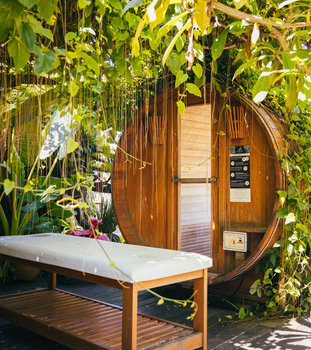 Camilla de masajes junto a una sauna de barril rodeada de lianas