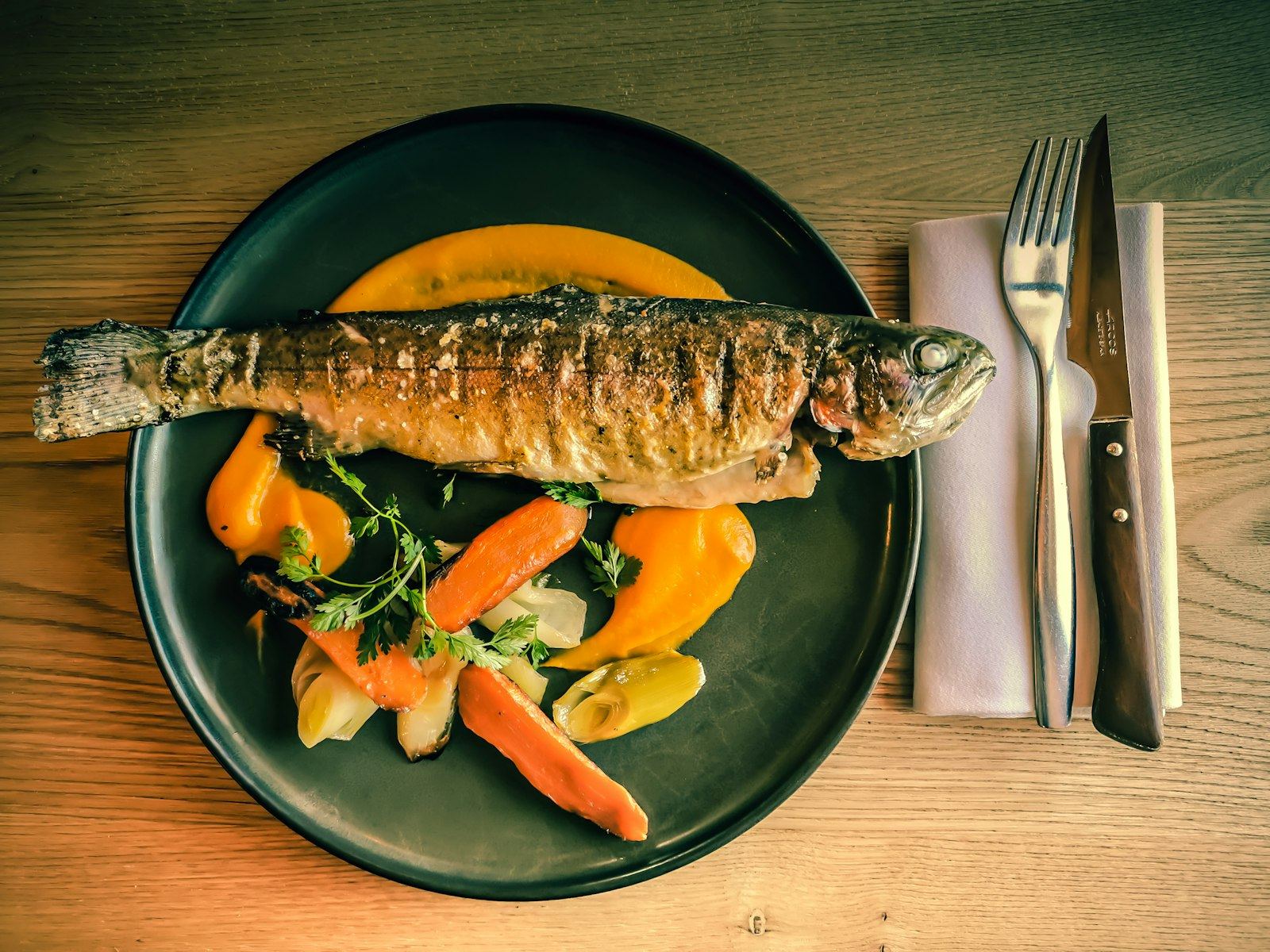 Pescado de río a la parrilla con verduras sobre plato oscuro